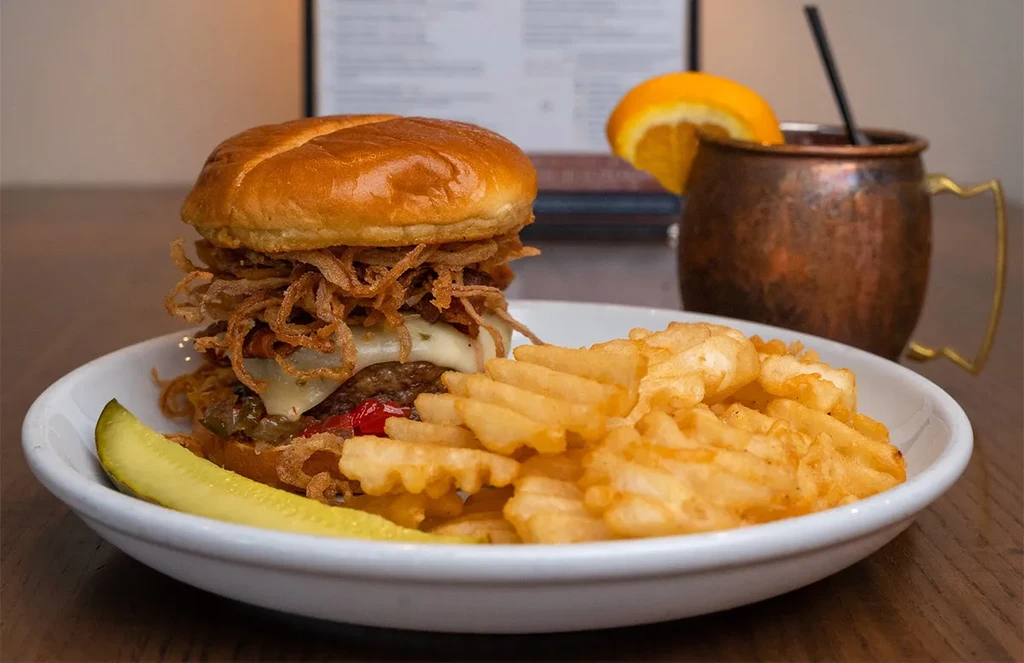 Gourmet burger, waffle fries, pickle, and copper mug drink.