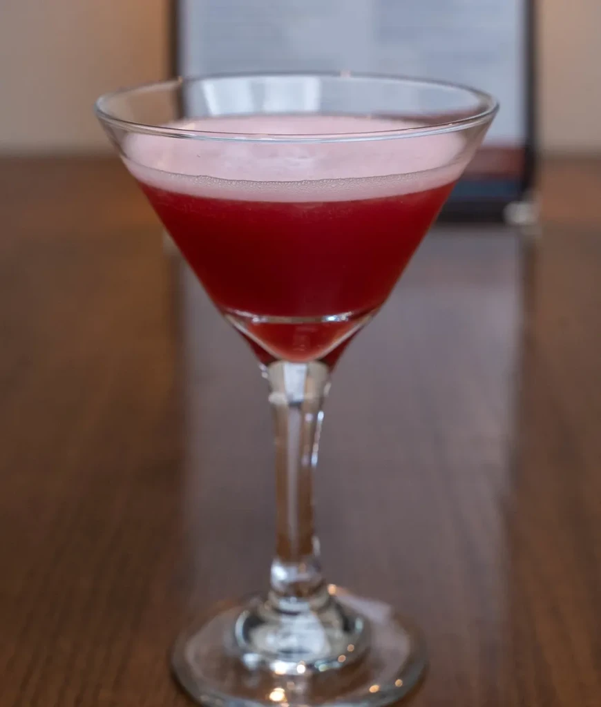 Vibrant reddish-pink frothy cocktail in a martini glass on wood.