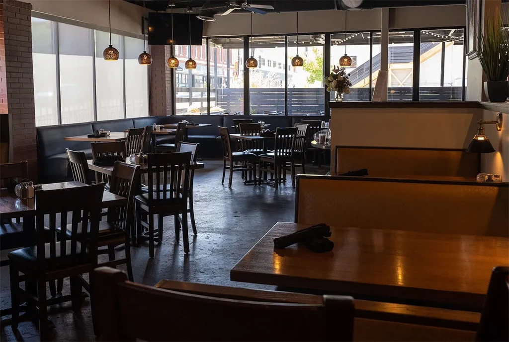 Empty modern restaurant interior with dark booths, wooden tables, and exposed brick.