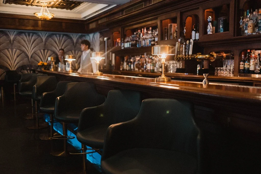 Dimly lit, elegant bar with illuminated counter and two staff.