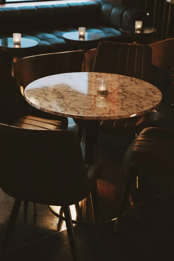 Dim restaurant interior with marble table, lit candle, chairs, and booth.