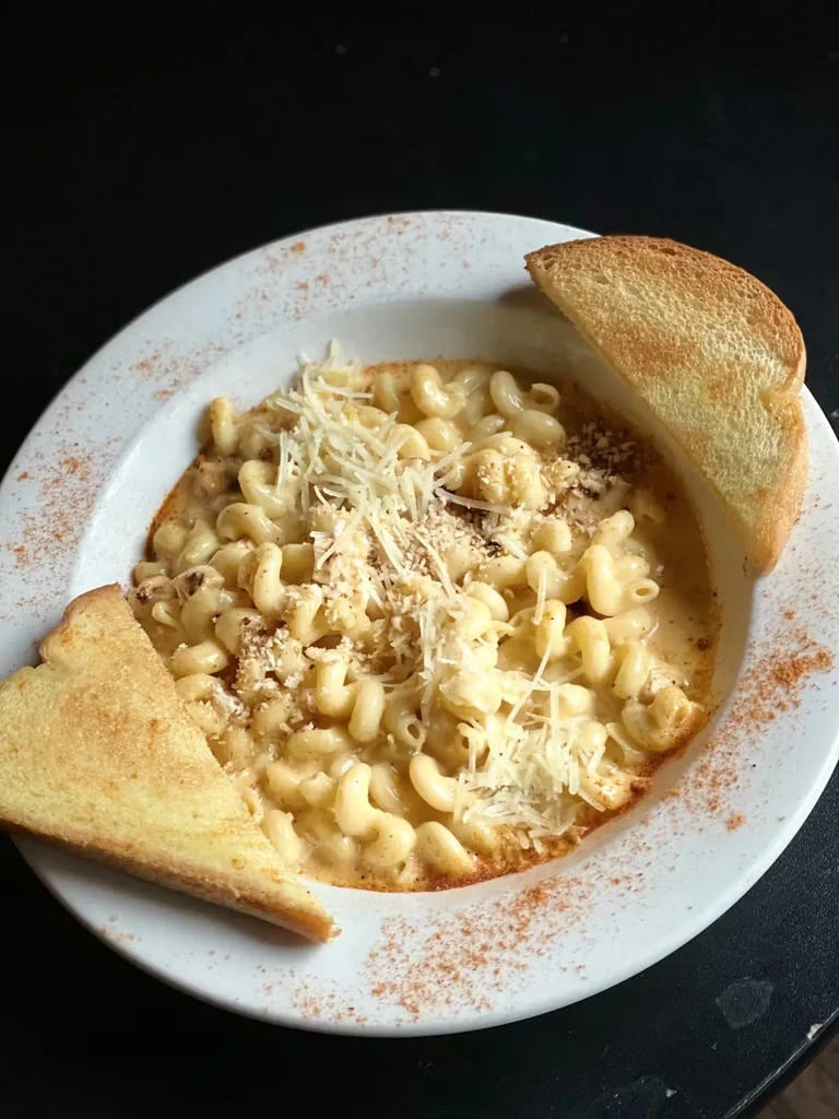 Creamy macaroni and cheese topped with shredded cheese, breadcrumbs, and toast.