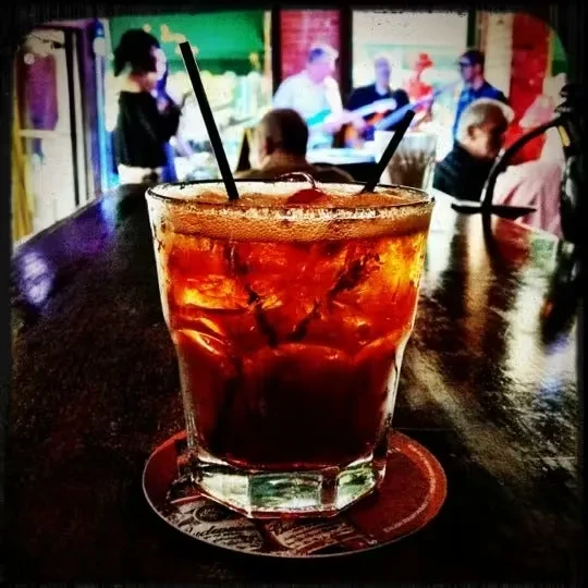 Dark amber drink with ice, straws, blurred band in background.
