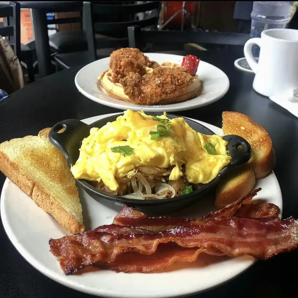 Close-up of two plates: scrambled eggs, bacon, toast, chicken, waffles.