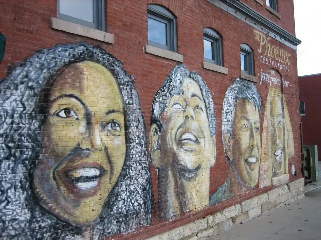 Colorful mural of joyful faces on brick building with 'The Phoenix Restaurant' sign.