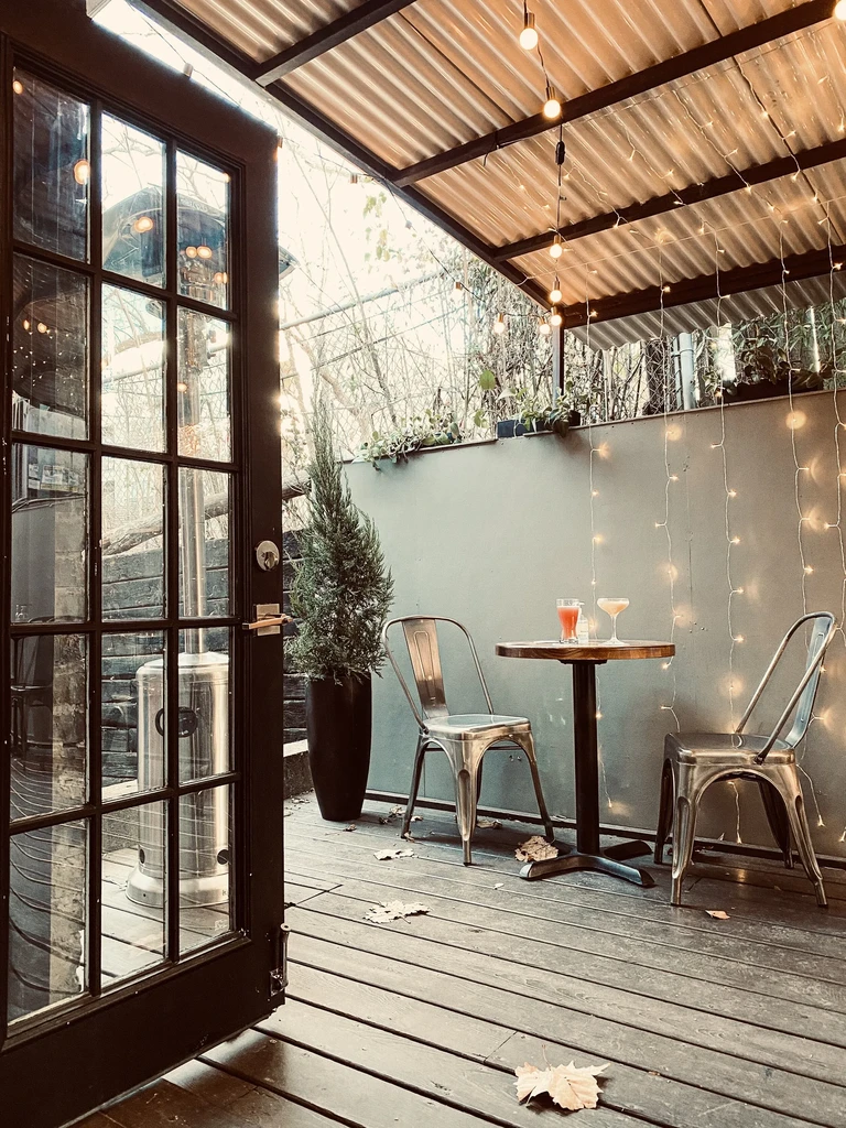 Patio deck with two cocktails, string lights, metal chairs.
