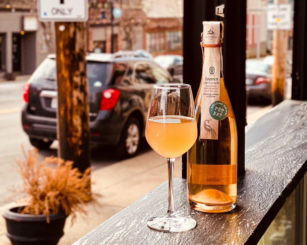 Wine glass and Pet Nat bottle on urban bar overlooking street.