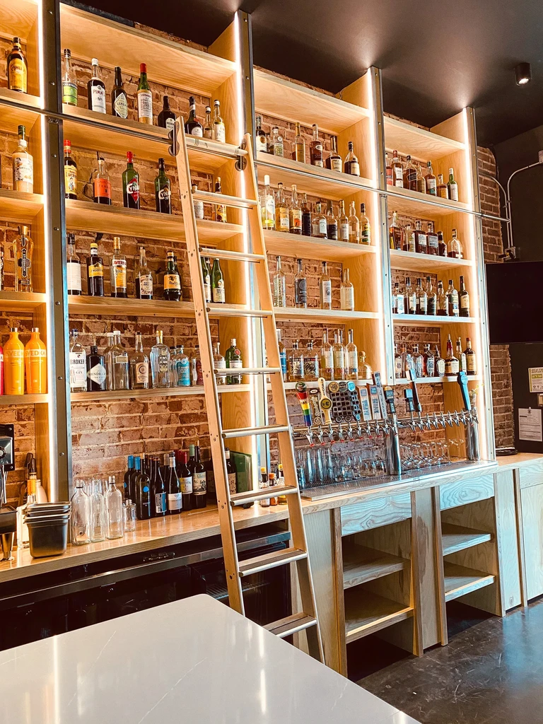 Expansive bar with glowing liquor shelves, beer taps, and rolling ladder.