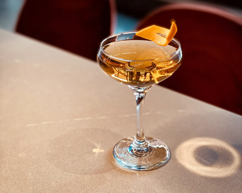 Amber cocktail in a coupe glass with orange peel garnish.