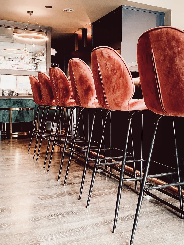 Five empty salmon-pink velvet bar stools at a modern bar.