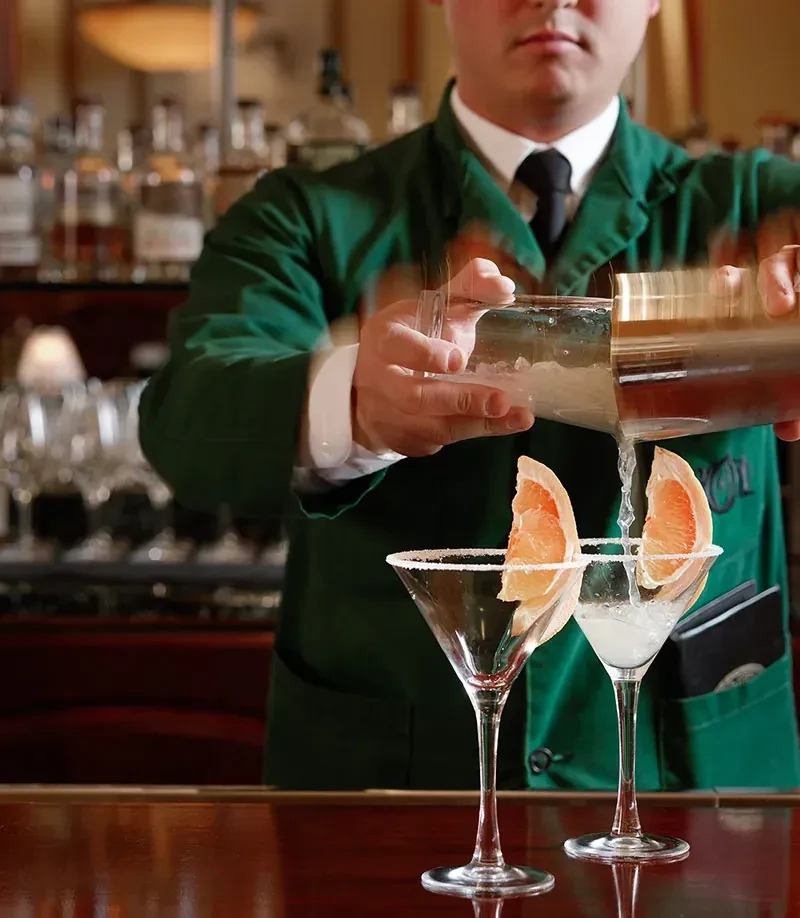 Bartender pouring cocktails into two sugar-rimmed martini glasses with grapefruit.