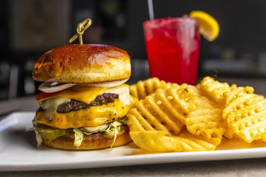 Double cheeseburger, waffle fries on plate, blurred red drink.