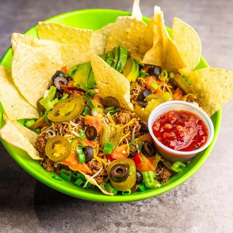 Loaded nachos in green bowl with meat, cheese, jalapeños, and salsa.