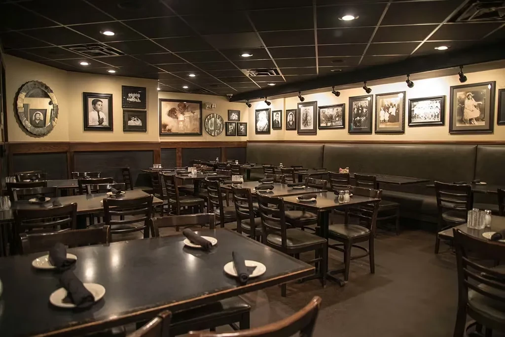 Empty restaurant dining room with dark tables, set plates, and framed photos.