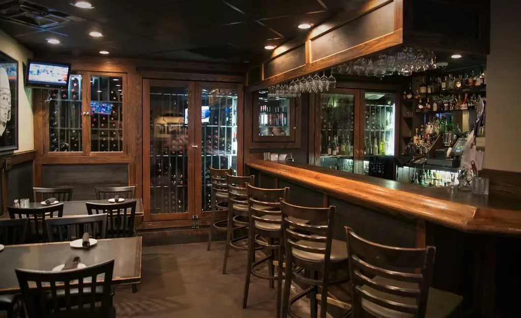 Upscale restaurant bar with wooden accents, wine storage, and sports TVs.