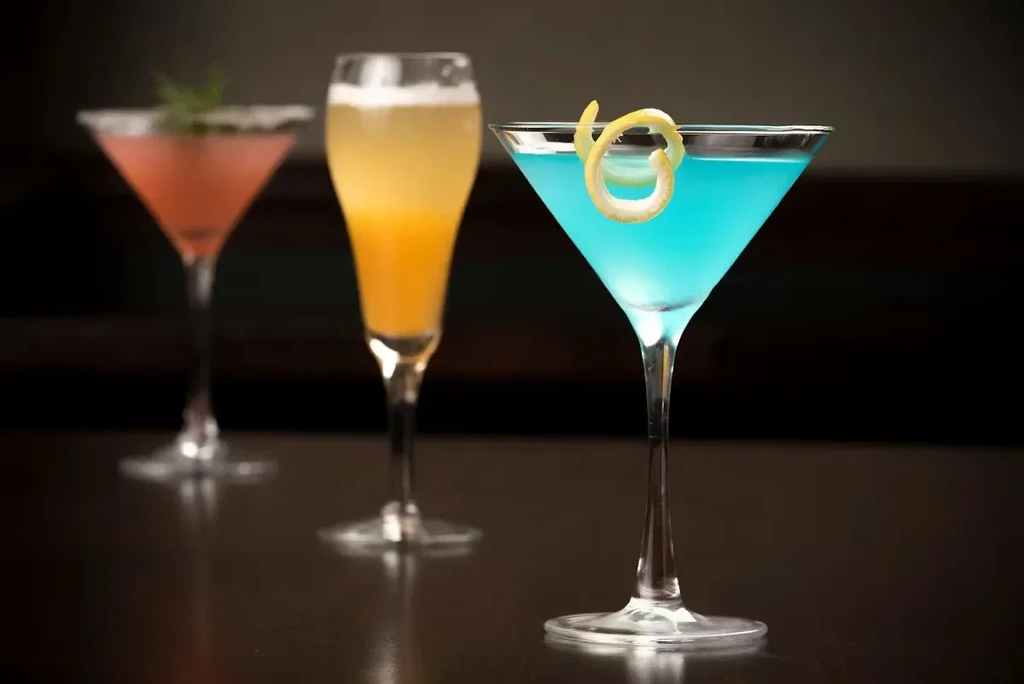 Three alcoholic cocktails on a dark surface, focused blue martini.
