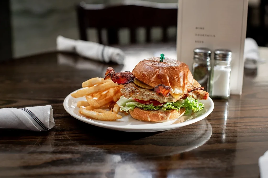 Close-up of a layered burger and crispy fries on a white plate.