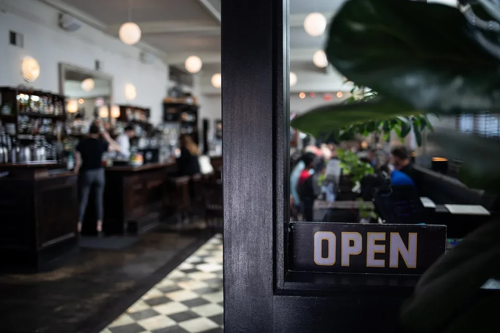 Focused 'OPEN' sign on door, blurred active bar interior beyond.