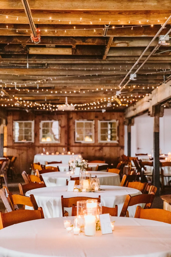 Elegant banquet hall with candlelit tables, fairy lights, and wooden beams.