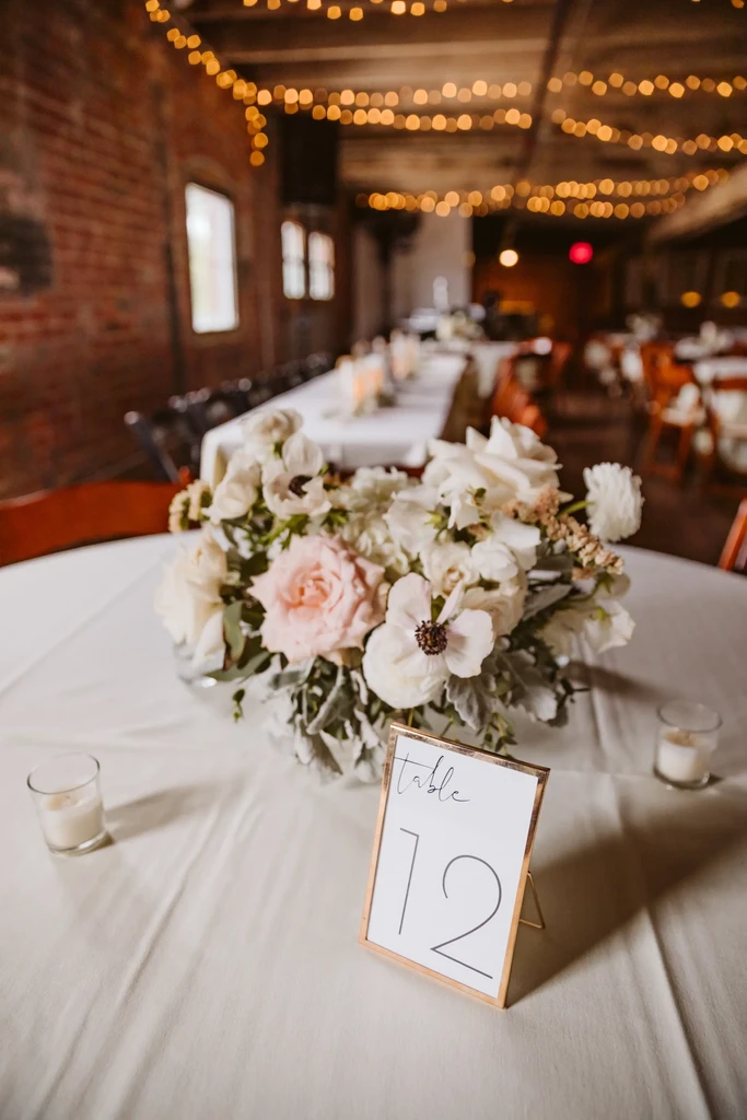 A set table with white and pink floral centerpiece and 'Table 12' sign.