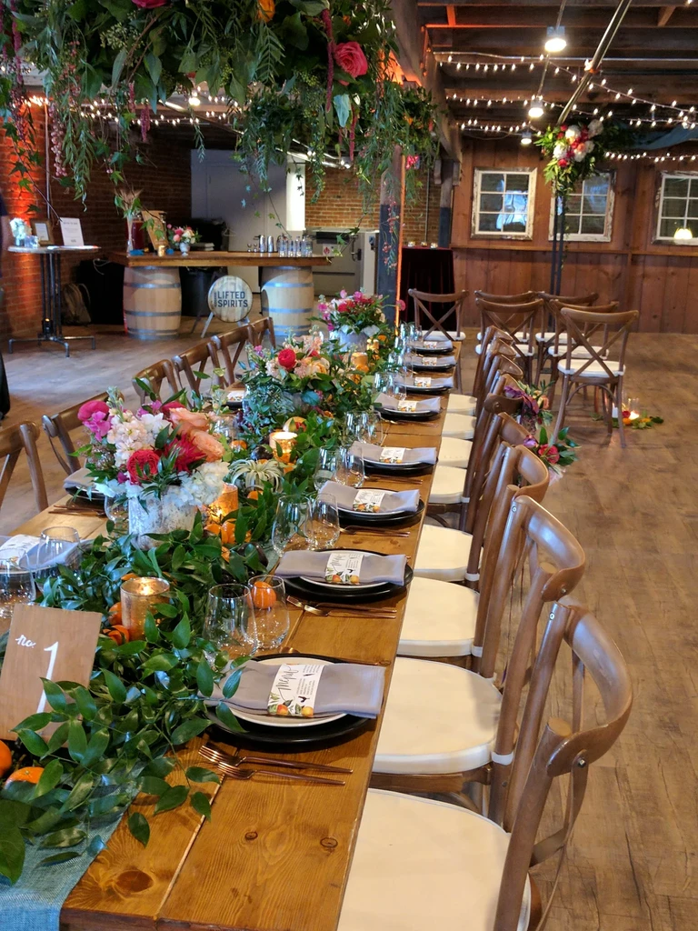 Long dining table with greenery, colorful flowers, candles, and place settings.