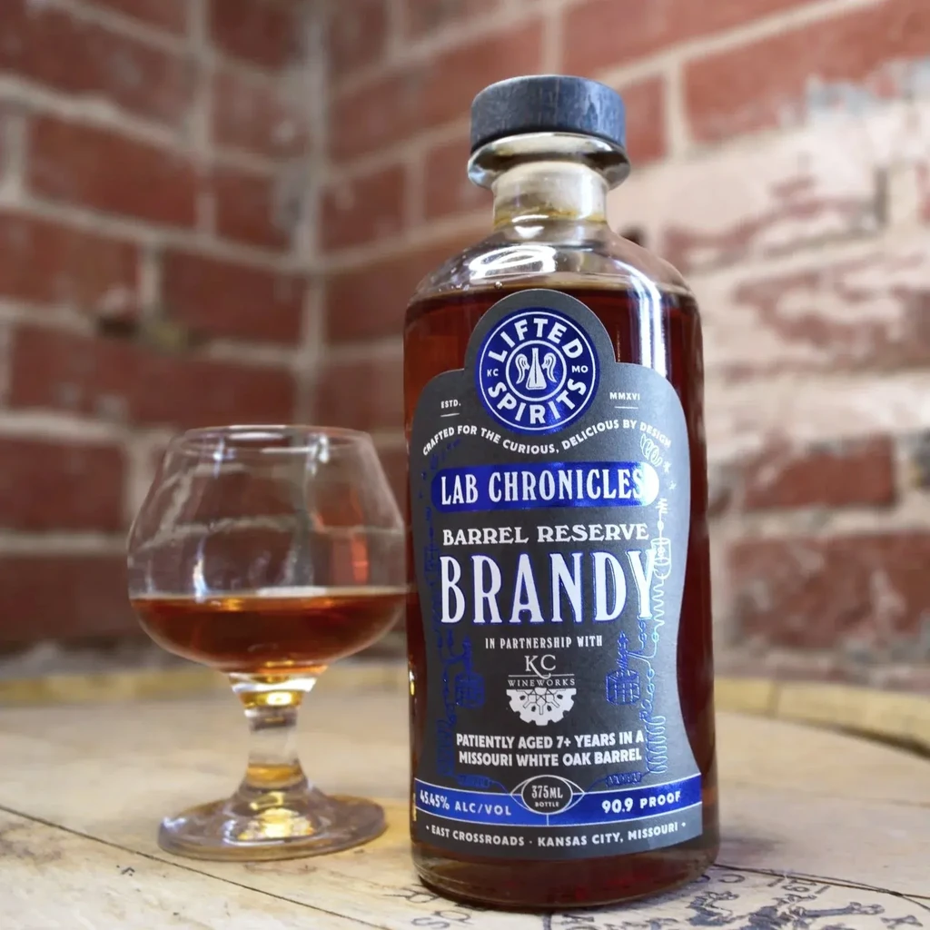 Lifted Spirits brandy bottle and snifter on wood surface, brick wall.