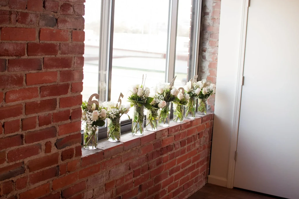 Interior brick wall, window, and white rose bouquets with gold numbers.