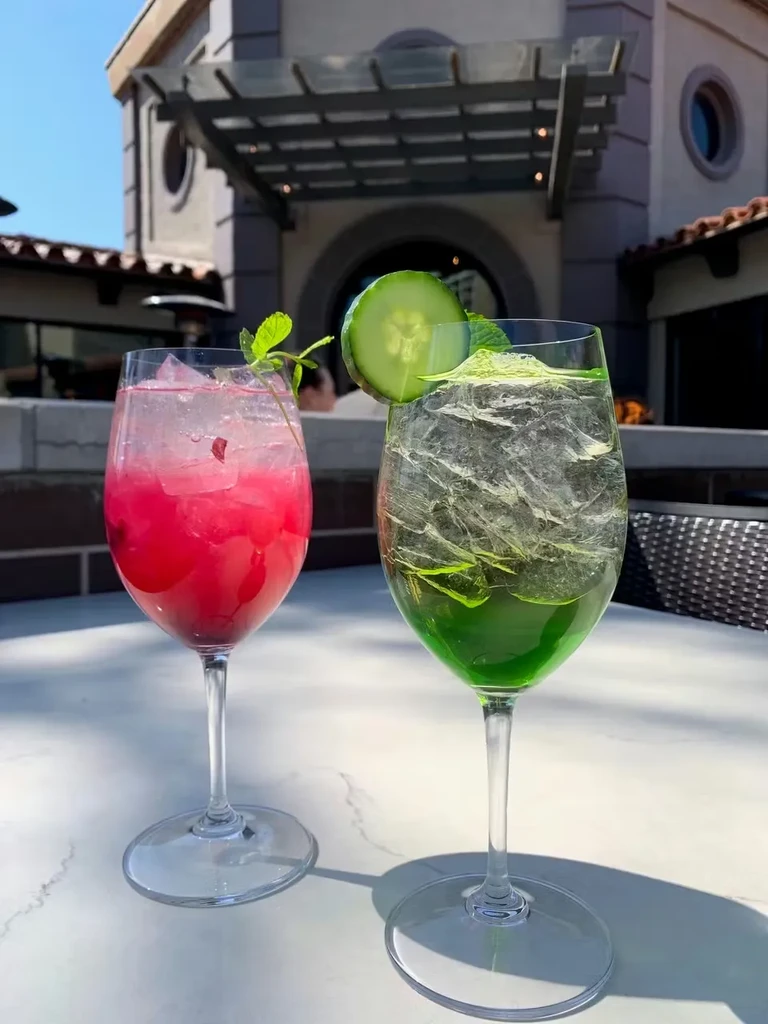 Two red and green garnished cocktails on a sunny outdoor patio.