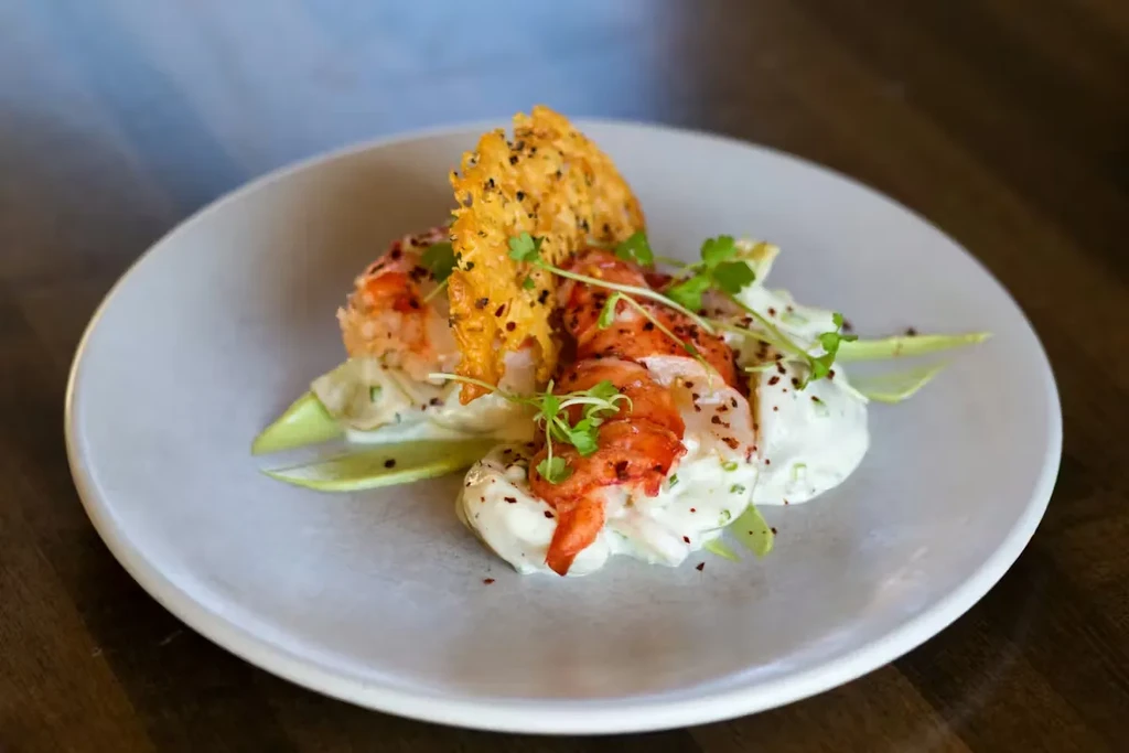 Orange-red seafood, creamy sauce, green garnishes, and a large seeded crisp.