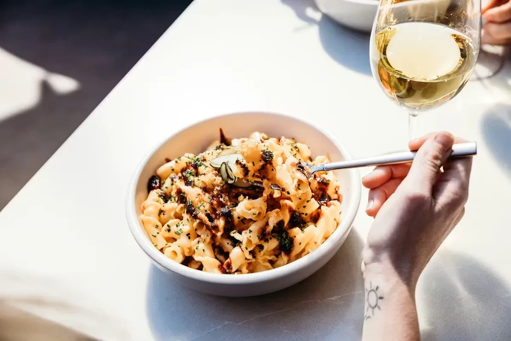 Close-up of mac and cheese with herbs, fork, wine, sun tattoo.