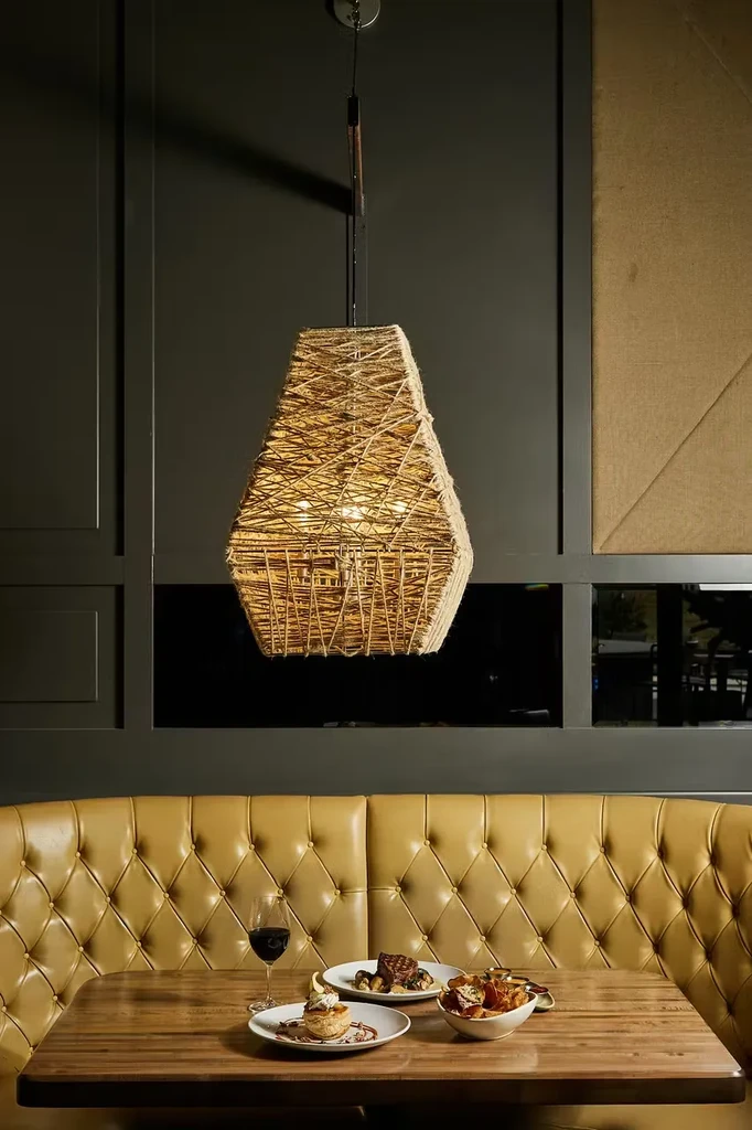 Restaurant table with food, wine, yellow booth, and woven pendant light.