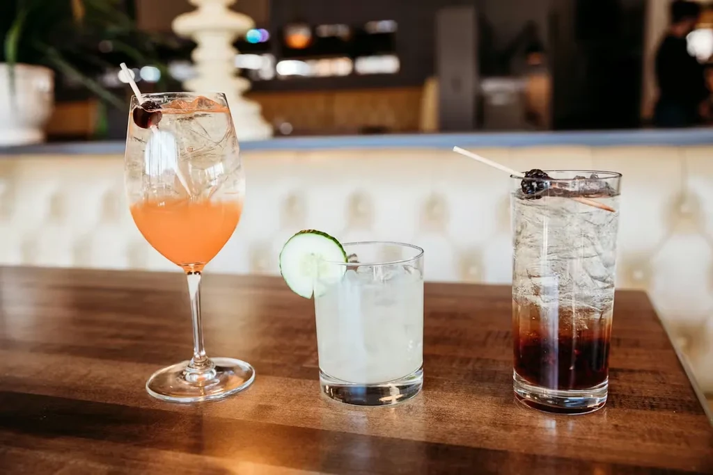 Three colorful, garnished drinks on a wooden bar counter.