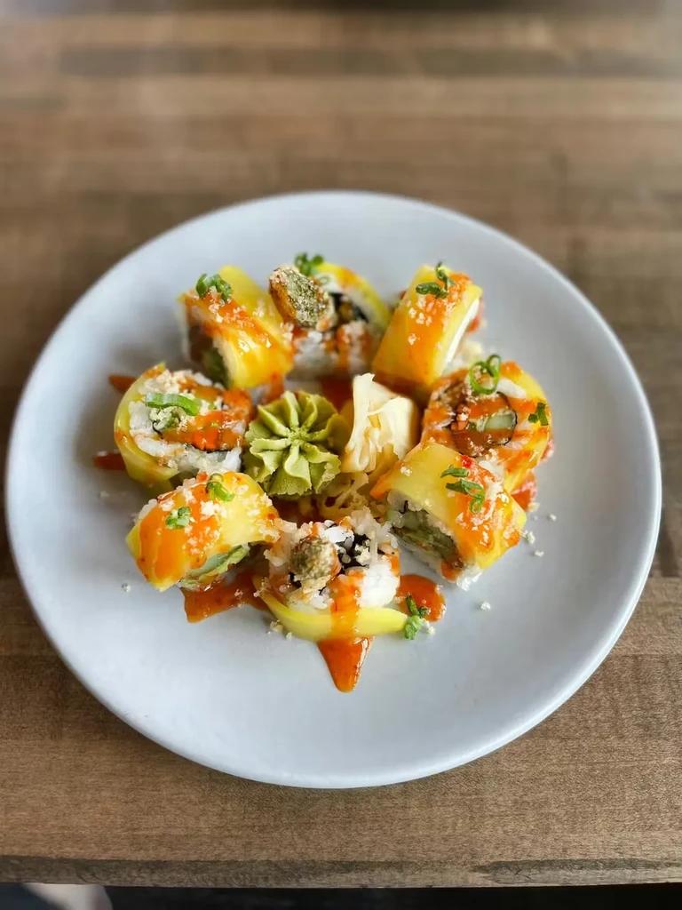 Sushi rolls with yellow topping, orange sauce, wasabi, and pickled ginger.