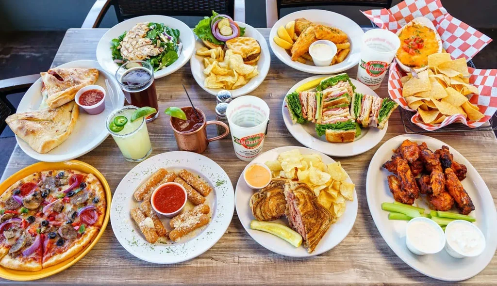 Numerous casual restaurant dishes and drinks on a wooden table.