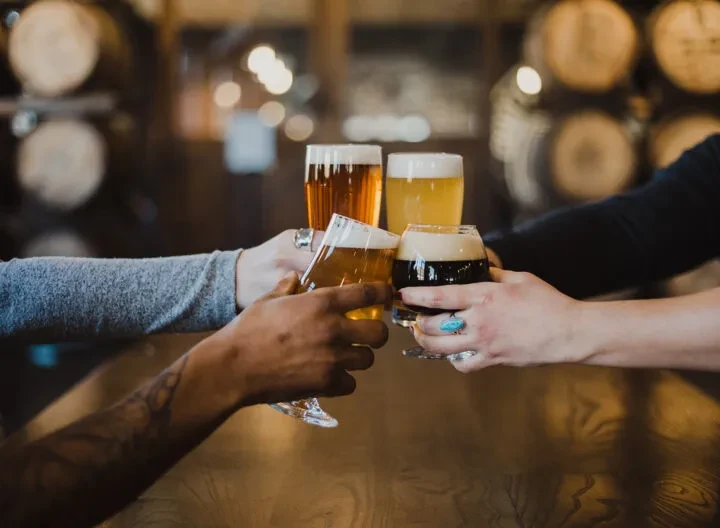 Four diverse hands clinking different beers in a brewery toast.