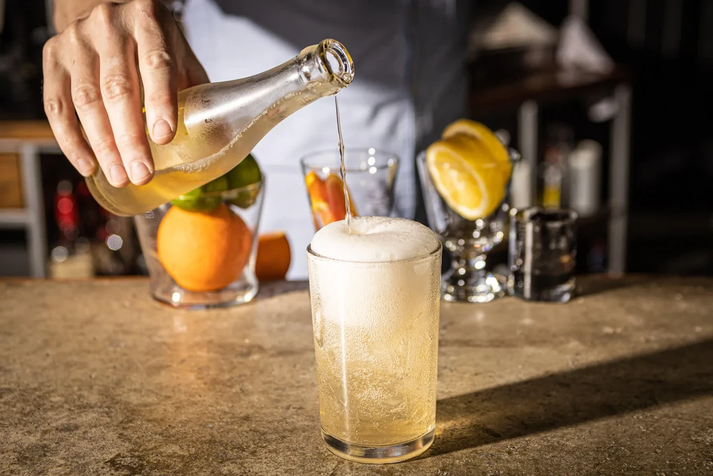 Hand pours golden liquid, creating foam in a cold glass at a bar.