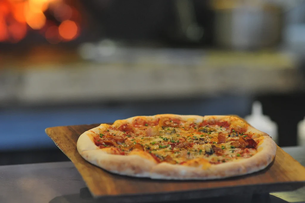 Rectangular pizza with cheese, meat, mushrooms, herbs on wooden peel.
