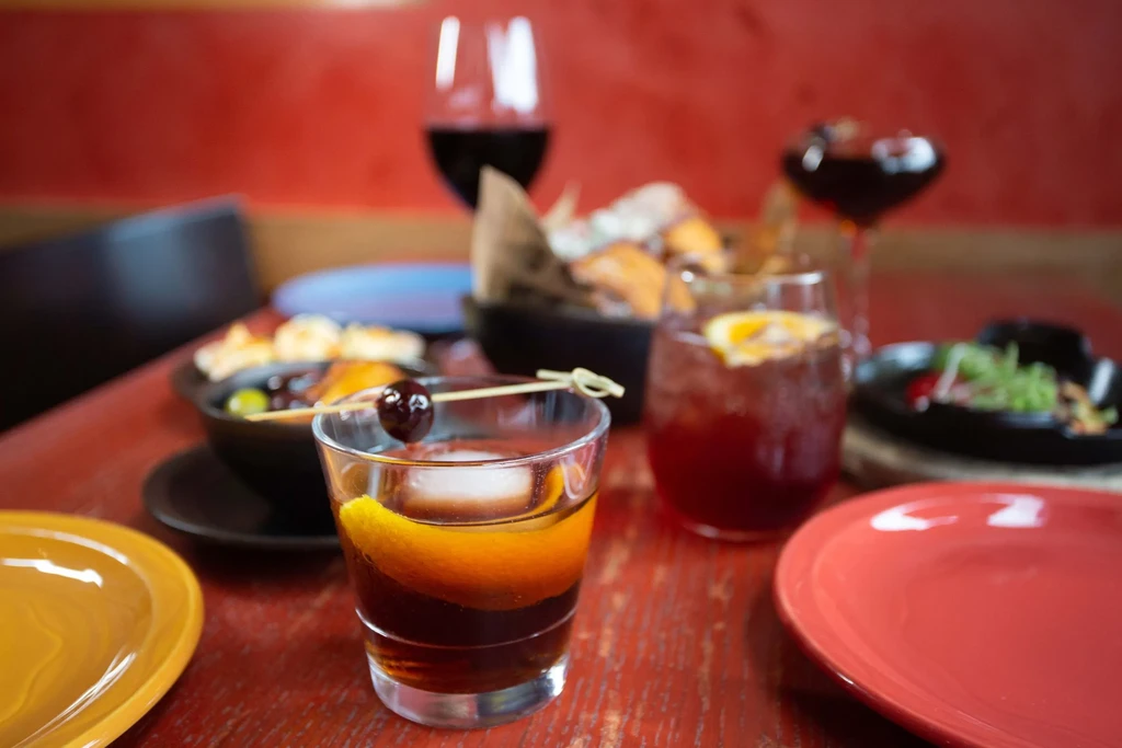 Amber cocktail with spherical ice, orange peel, cherry on a wooden table.