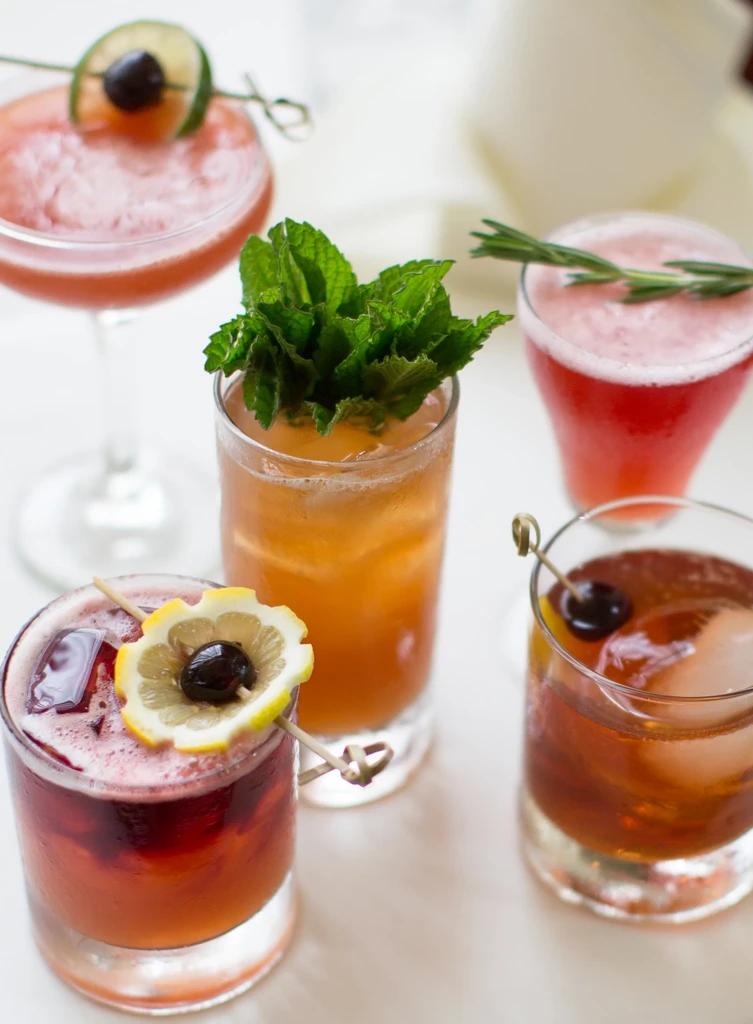Five colorful, garnished cocktails in varied glassware on a table.