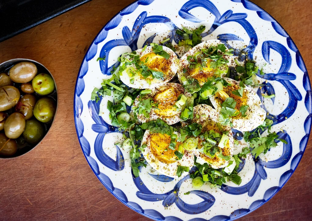 Halved hard-boiled eggs with herbs, spice, and olives on wood.