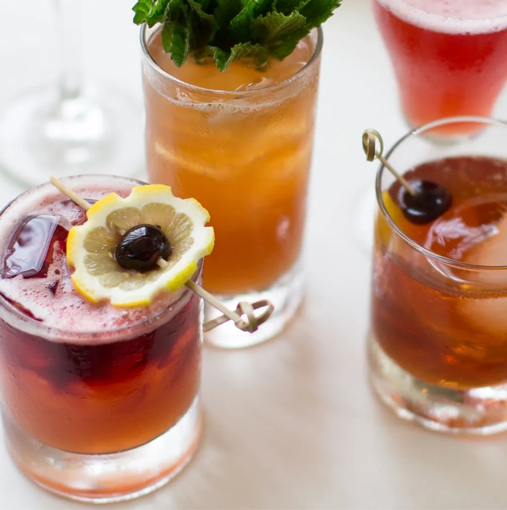 Four brightly colored cocktails with various garnishes on a light surface.