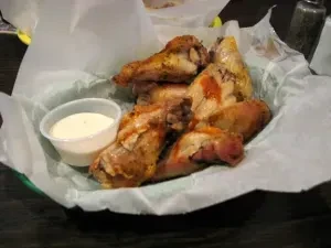 Seasoned chicken wings in a basket with white dipping sauce.
