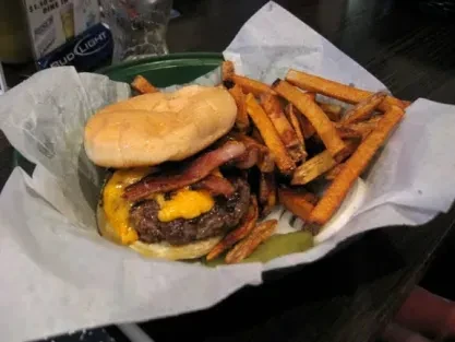 A bacon cheeseburger served with a large pile of sweet potato fries.