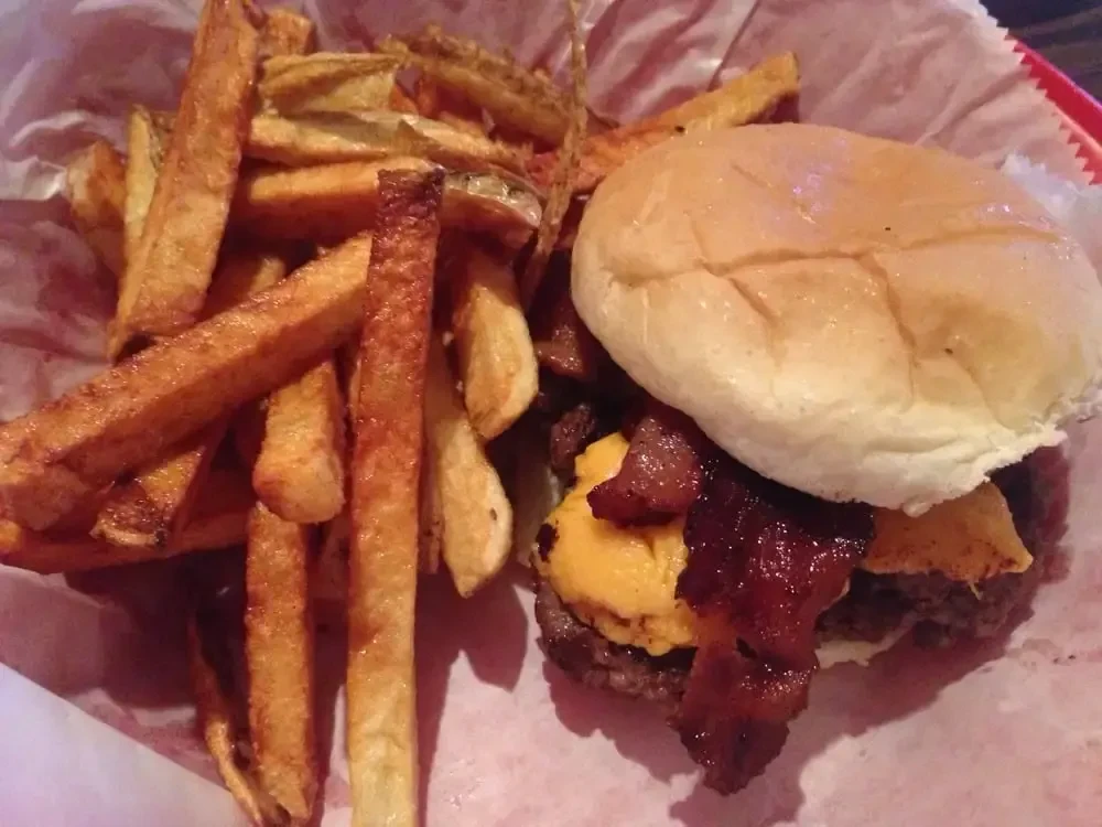 Hamburger with bacon, cheese, and hand-cut fries in a red basket.