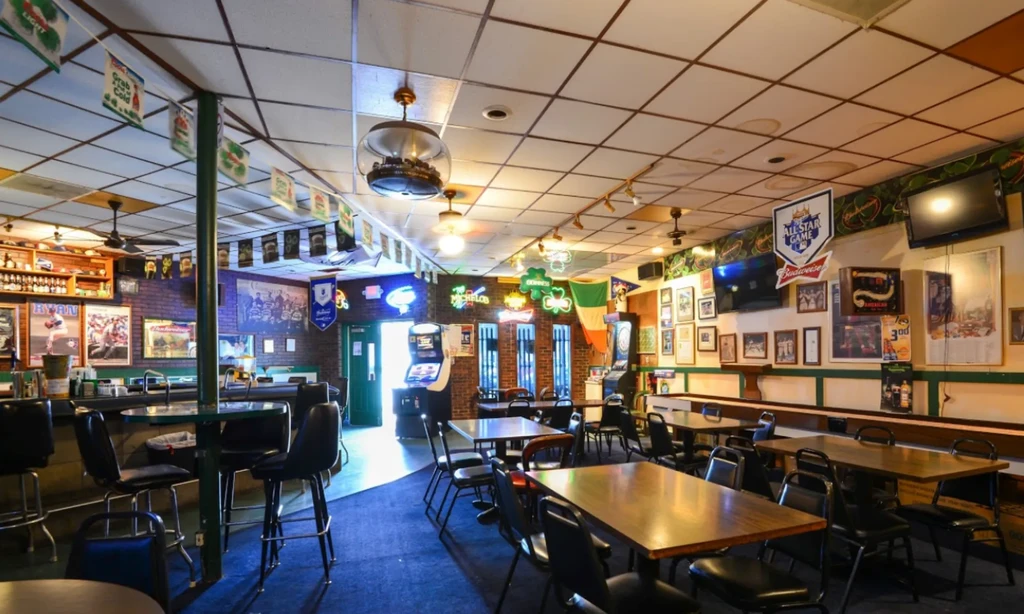 Casual pub interior with a bar, tables, Irish flag, and shuffleboard.