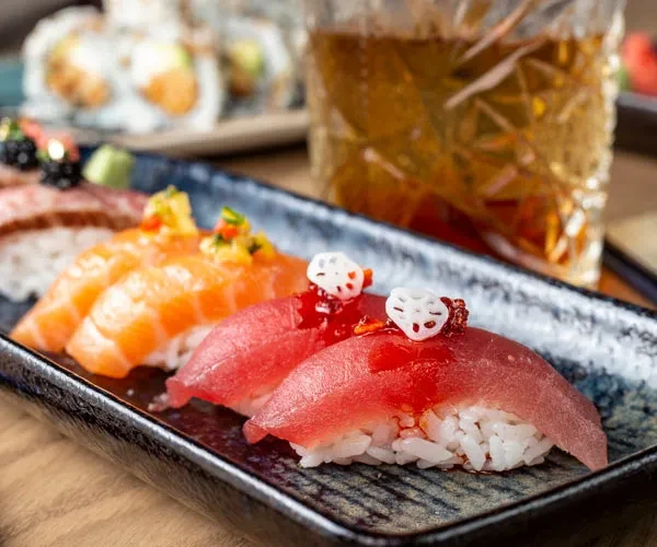 Artfully arranged tuna and salmon nigiri with garnishes on dark plate.