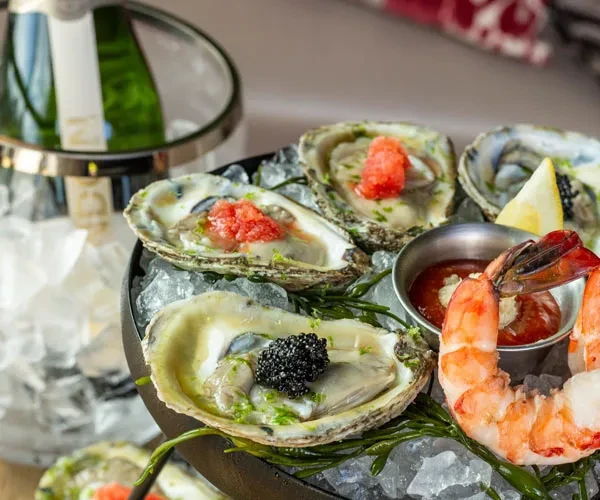 Black platter with oysters, shrimp, caviar, lemon, and cocktail sauce.