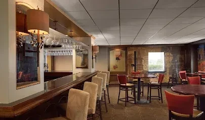 Warmly lit, empty bar lounge with a wooden bar and tables.