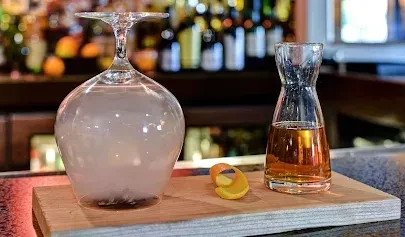 Two glasses: inverted mist glass, carafe with amber spirit, orange peel.