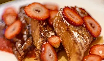 French toast slices with strawberries, powdered sugar, and red sauce.